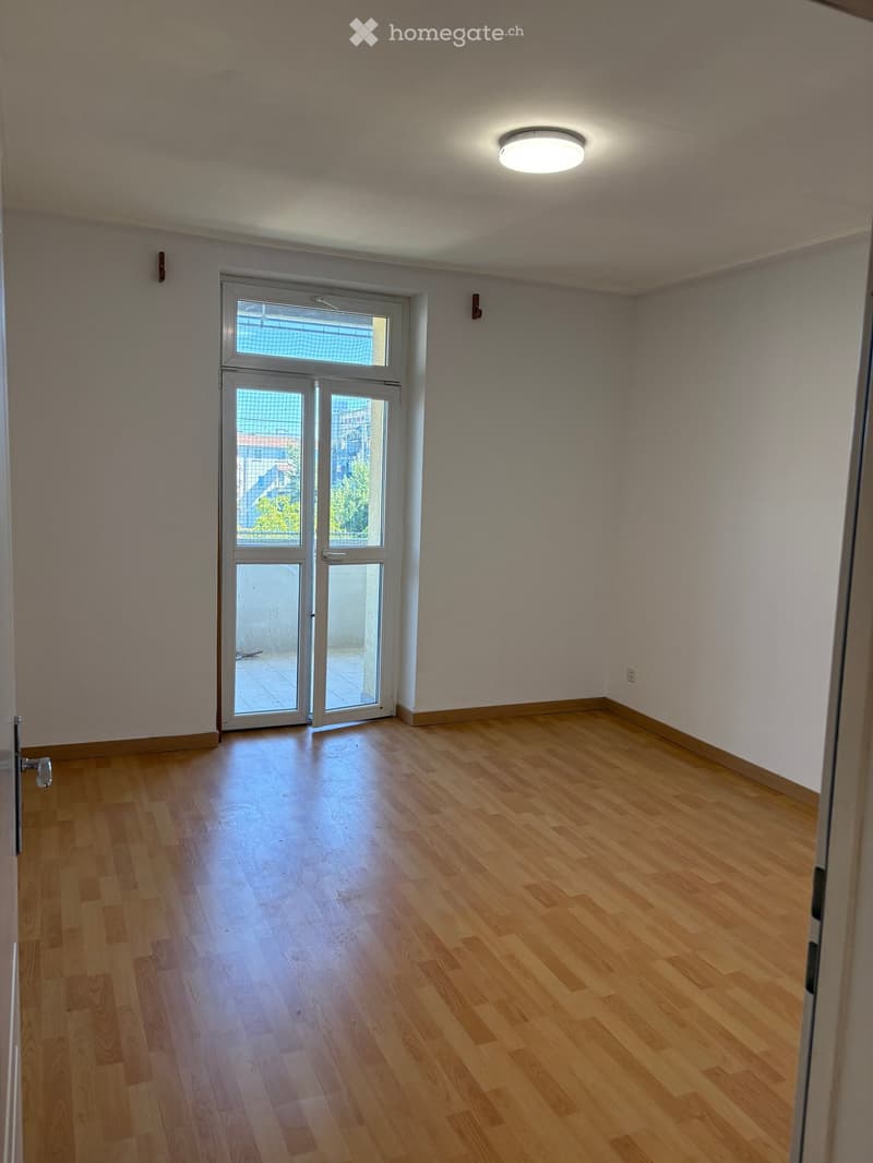 Empty room with wooden flooring, white walls, and a large glass door leading outside.