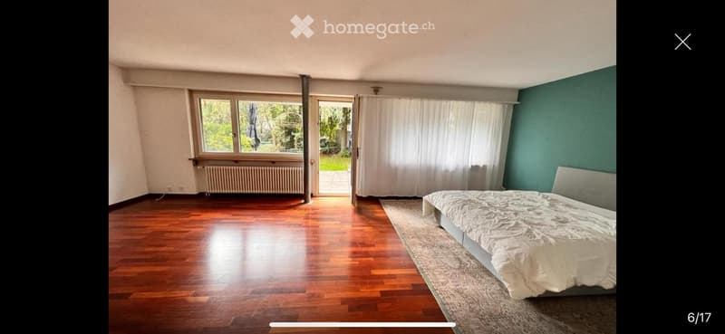 Bright bedroom with wooden flooring, large windows, and a bed with white bedding.