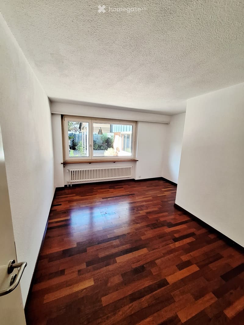 Empty room with wooden flooring, white walls, and a large window with a radiator below it.