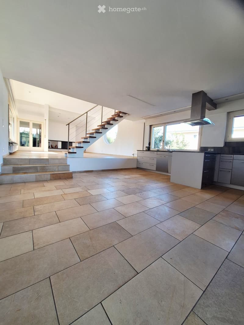 Empty kitchen with modern design, light-colored tiles, and a staircase leading to another level. No furniture or appliances are visible.