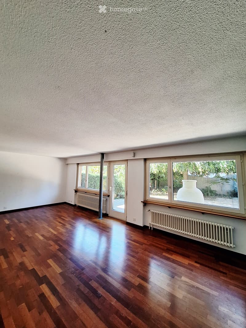 Empty room with wooden flooring, large windows, and radiators. No furniture or equipment present.