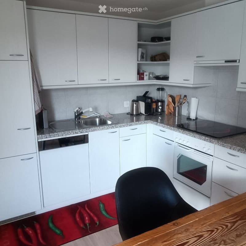 Modern kitchen with white cabinets, granite countertops, stainless steel appliances, and a wooden table with a black chair.