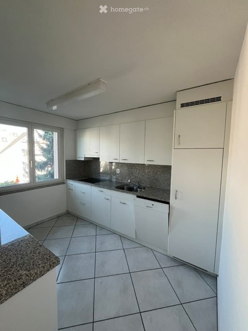 Modern kitchen with white cabinets, tiled floor, and stainless steel sink.