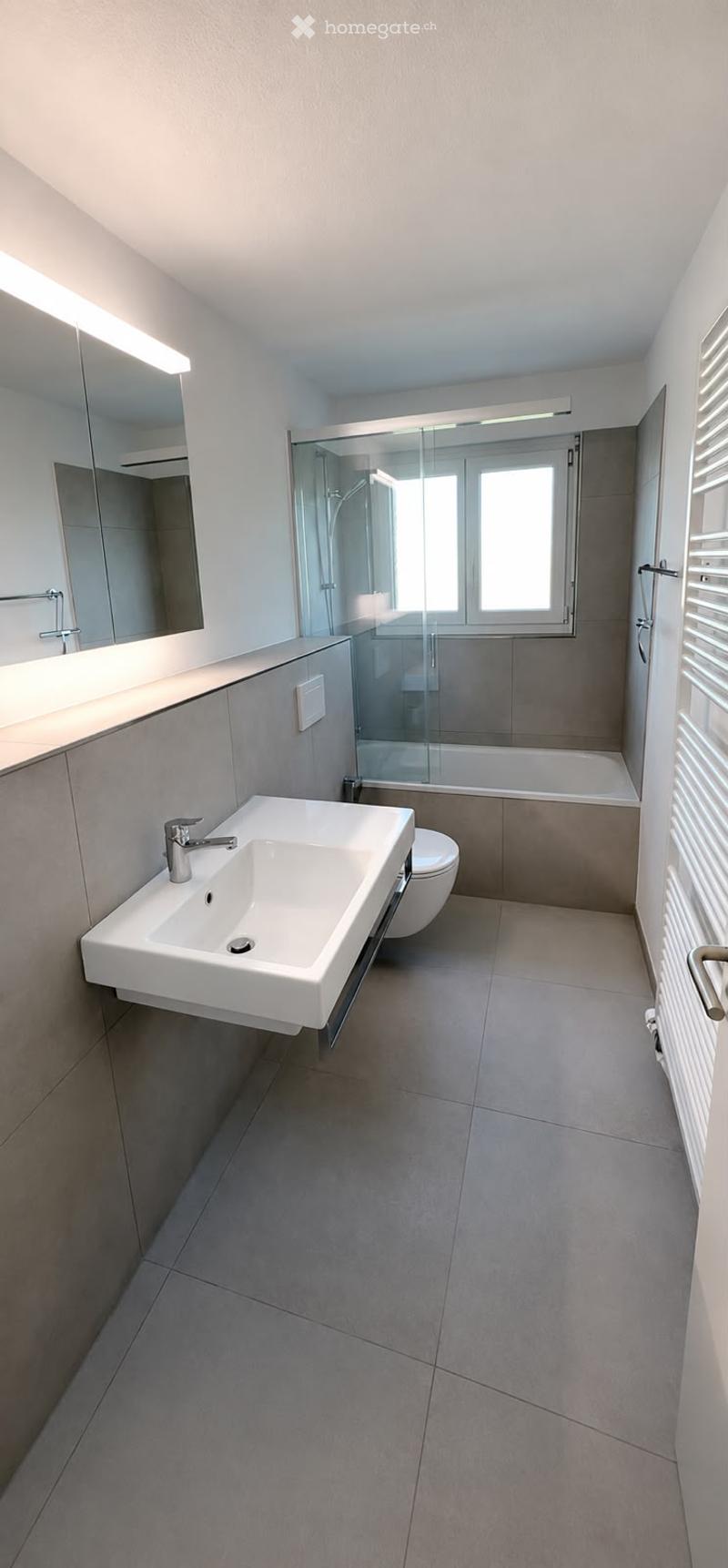 Modern bathroom with a white sink, chrome faucet, large mirror, toilet, bathtub, and glass-enclosed shower area.