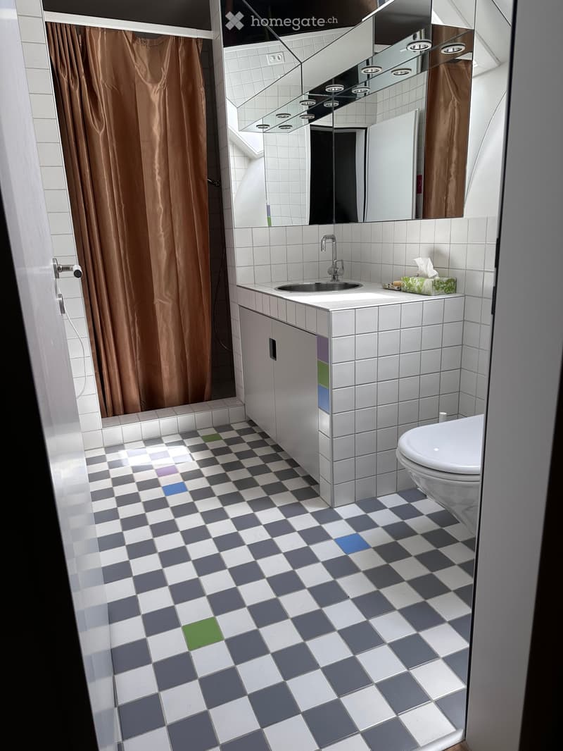 Modern bathroom with white tiled walls, a large mirror, a sink with a chrome faucet, a toilet, and a colorful checkered floor.