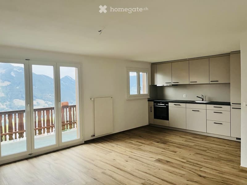 Modern kitchen with light-colored cabinets, wooden flooring, and large windows offering a scenic mountain view.