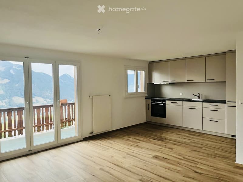 Modern kitchen with light-colored cabinets, wooden flooring, and large windows offering a scenic mountain view.