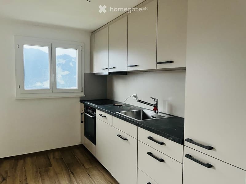 Modern kitchen with white cabinets, black countertop, stainless steel sink, and a view of mountains through the window.