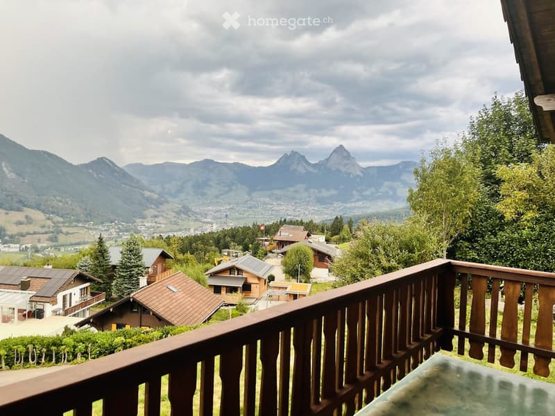 Balcony overlooking a scenic mountain landscape with houses and trees in the foreground.
