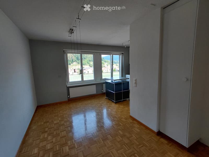 Bright, unfurnished room with wooden flooring, large windows, and a single storage unit. The space is clean and open, with natural light streaming in.