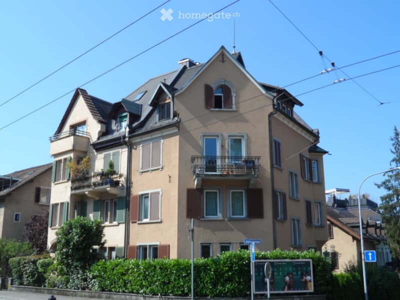 Multi-story residential building with beige facade, multiple windows, balconies, and shutters.