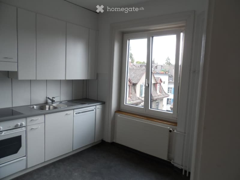Modern kitchen with white cabinets, stainless steel sink, oven, dishwasher, and a window overlooking a residential area.