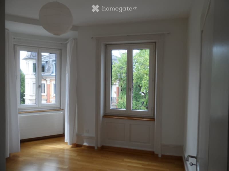 Empty room with wooden flooring, large windows, white walls, and a hanging paper lantern light fixture.