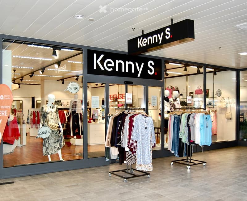 Retail store interior with clothing racks, mannequins, and handbags displayed. The store is well-lit with a modern design and has a sign reading "Kenny S" above the entrance.