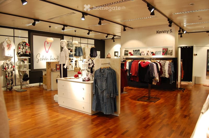 A well-lit clothing store with wooden flooring, clothing racks, mannequins, and shelves displaying various garments and accessories.
