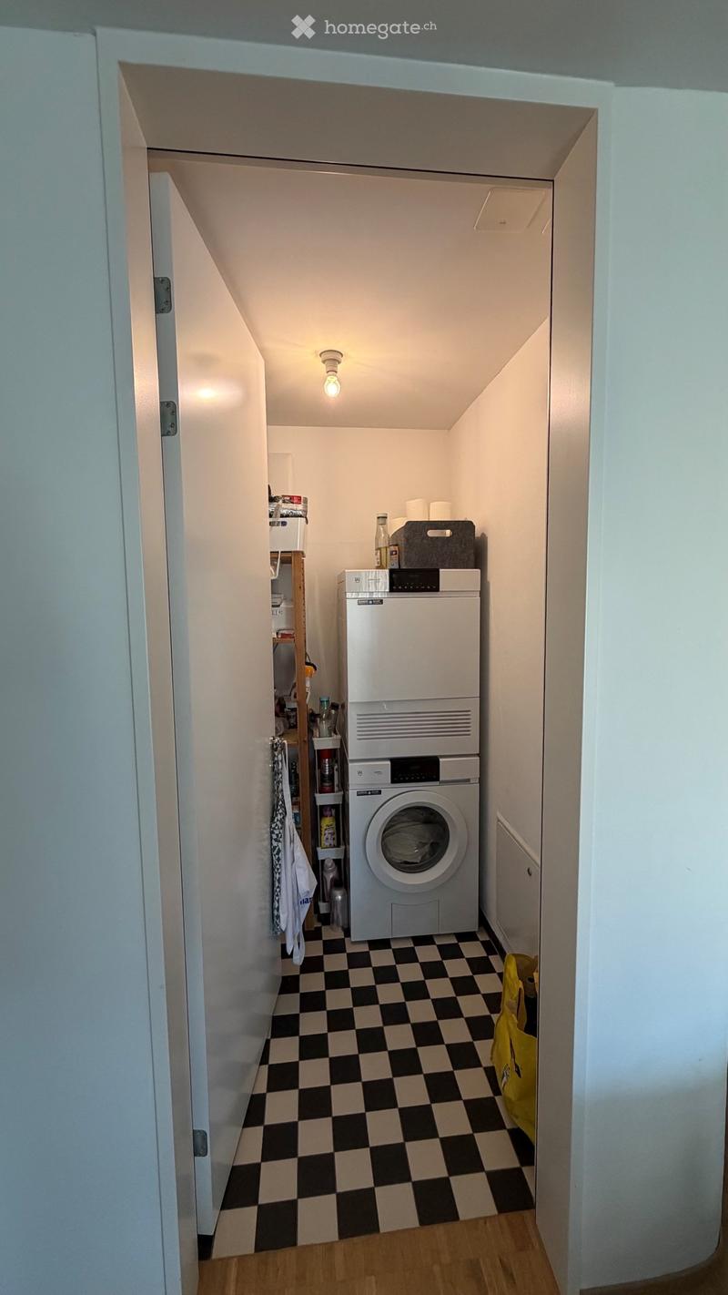 Small bathroom with a washing machine and dryer, checkered floor, shelves, and a towel hanging on the wall.