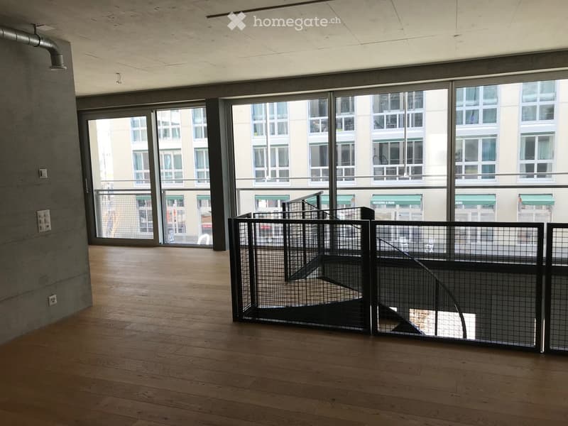 Empty room with wooden flooring, large glass windows, and a staircase with a metal railing.