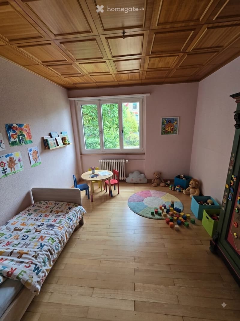 Brightly colored children's bedroom with a small bed, a round table with chairs, colorful toys, and artwork on the walls.