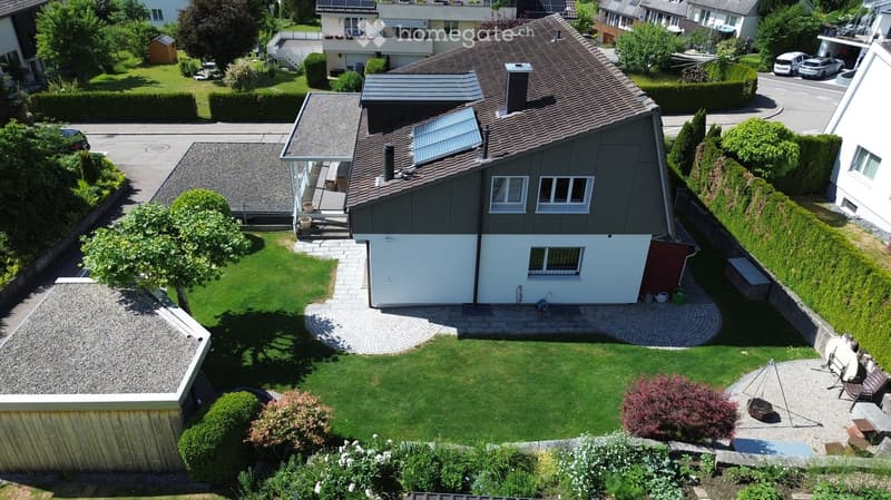 Aerial view of a residential house with a well-maintained garden, patio area, and surrounding neighborhood.