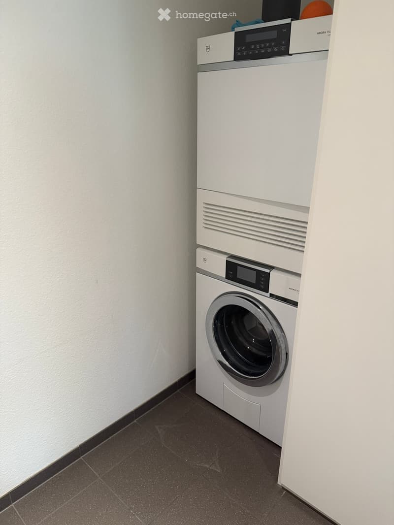 A compact laundry area with a white washing machine and dryer stacked vertically, featuring a control panel and a dark tiled floor.