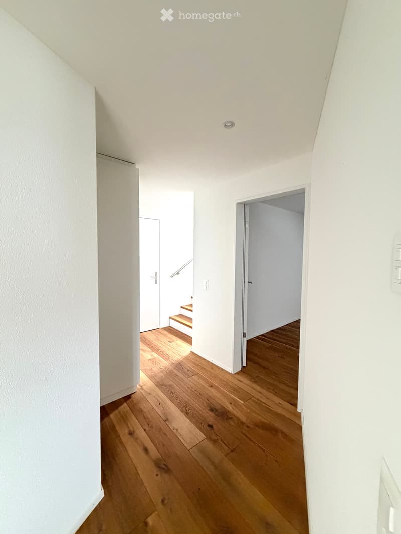 Bright hallway with wooden flooring, white walls, and a staircase leading upwards.