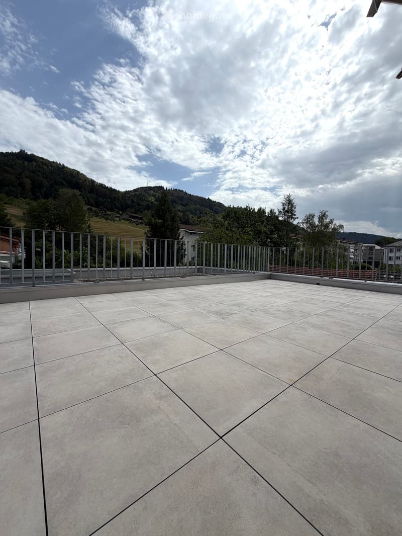Empty balcony with tiled floor, metal railing, and scenic mountain view in the background.