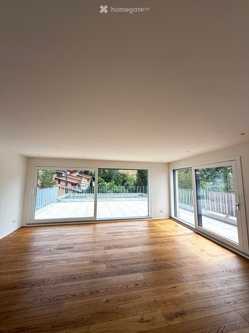 Empty room with wooden flooring, large sliding glass doors leading to a balcony or terrace, and natural light streaming in.