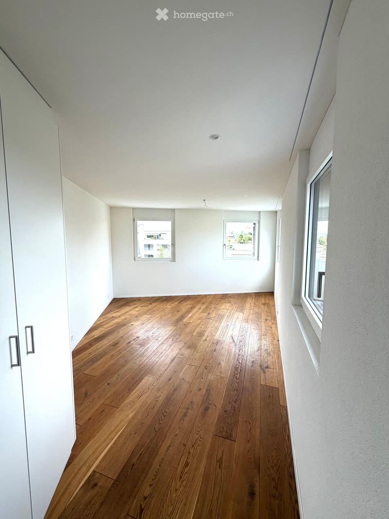 Empty room with wooden flooring, white walls, and large windows allowing natural light.