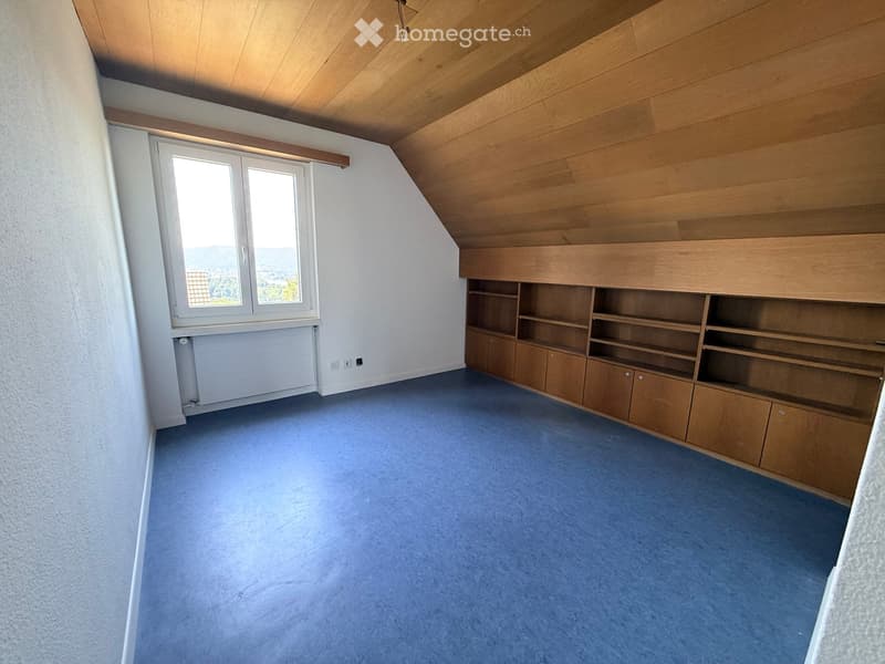 Empty room with wooden built-in shelving unit, blue carpet, large window with view, and wooden slanted ceiling.