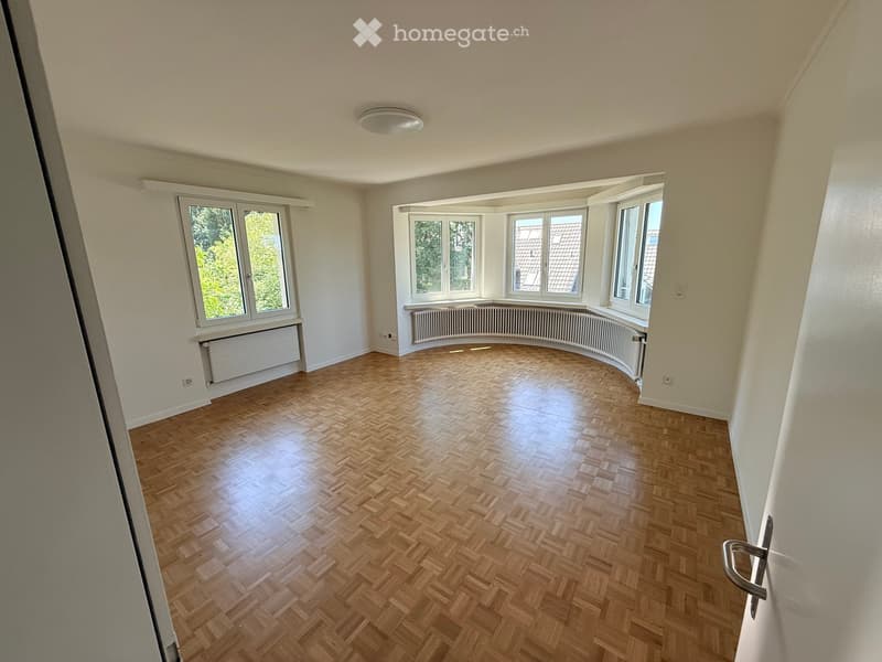 Empty room with wooden herringbone flooring, white walls, large windows, and radiators.