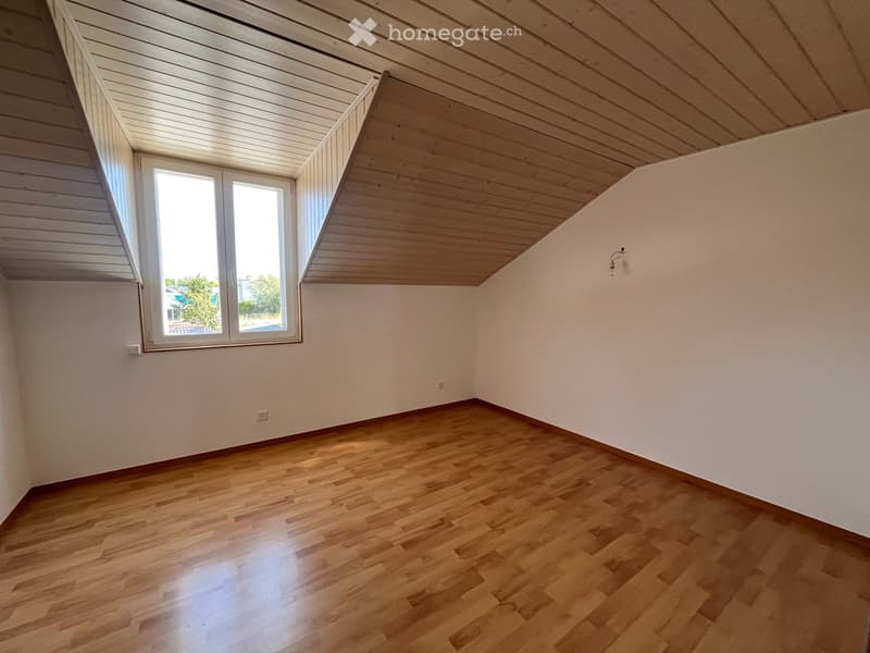 Empty attic room with wooden flooring, white walls, and a skylight window. The ceiling has exposed wooden beams and a sloped design.
