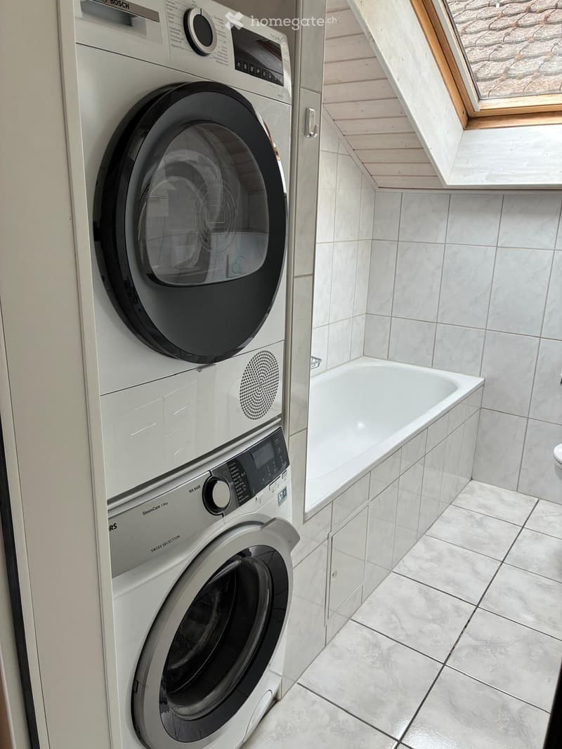 Modern bathroom with white tiled walls and floor, featuring a washing machine and a bathtub.