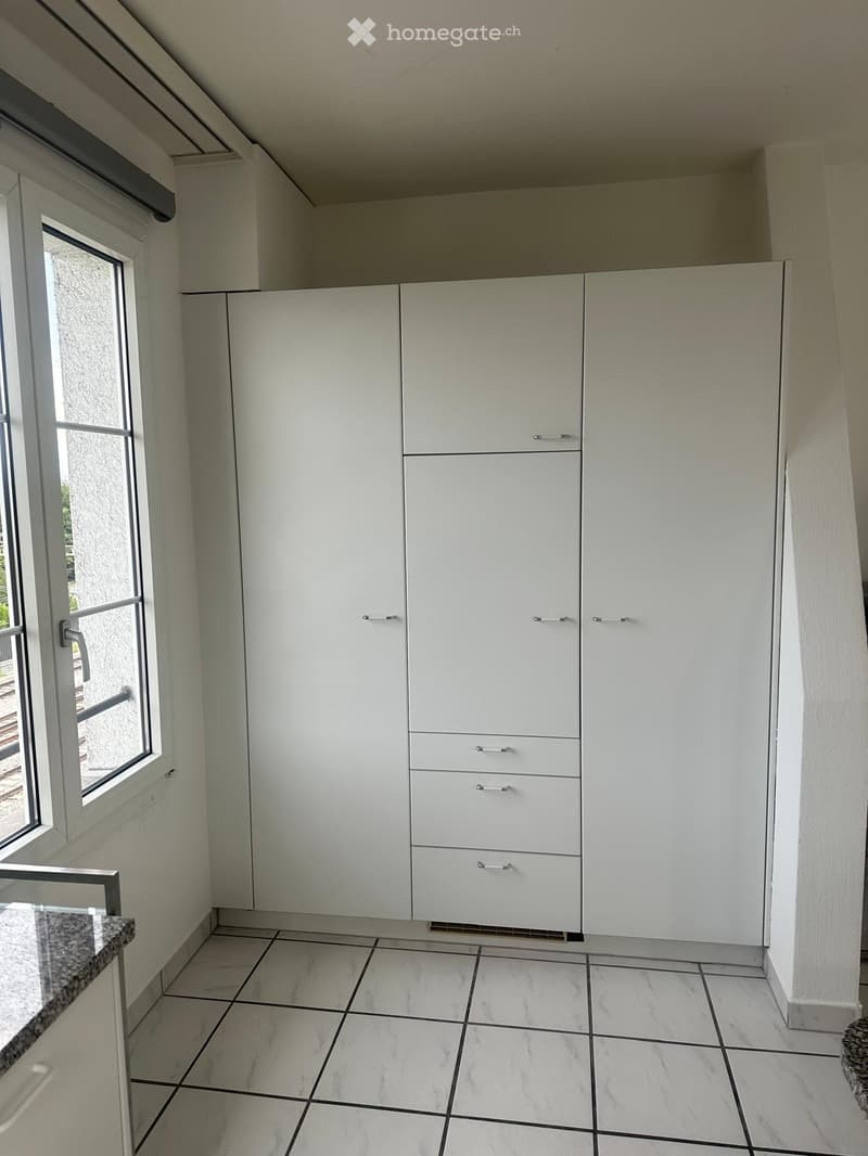 Modern kitchen with white cabinets, marble tiled floor, and a large window providing natural light.