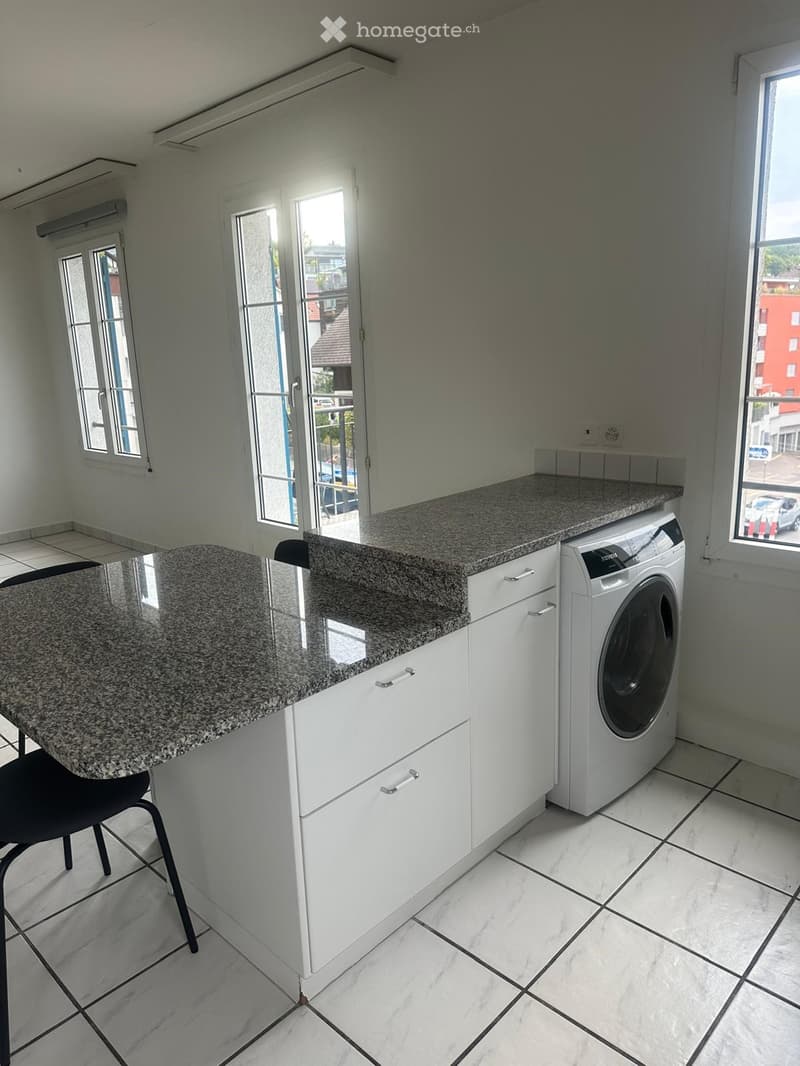 Bright, modern kitchen with white cabinets, granite countertops, a washing machine, and a black chair.