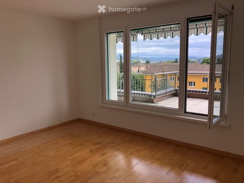 Empty room with wooden flooring and large windows offering a view of a balcony and outdoor area.