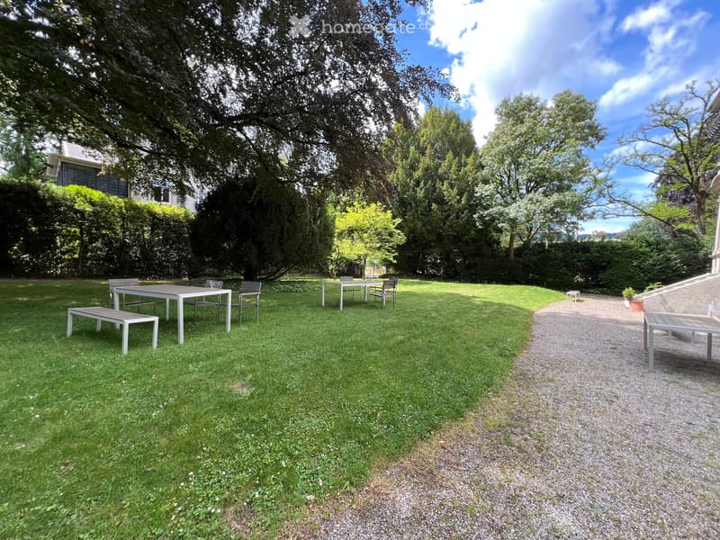 Well-maintained garden with a grassy lawn, a gravel pathway, and outdoor furniture including tables, chairs, and benches.