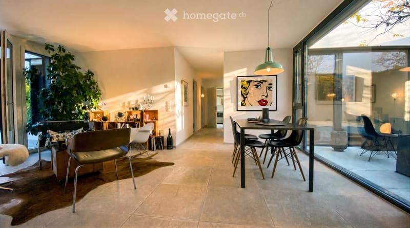 Modern living and dining area with large windows, a sofa, chairs, a dining table, pendant light, and artwork.