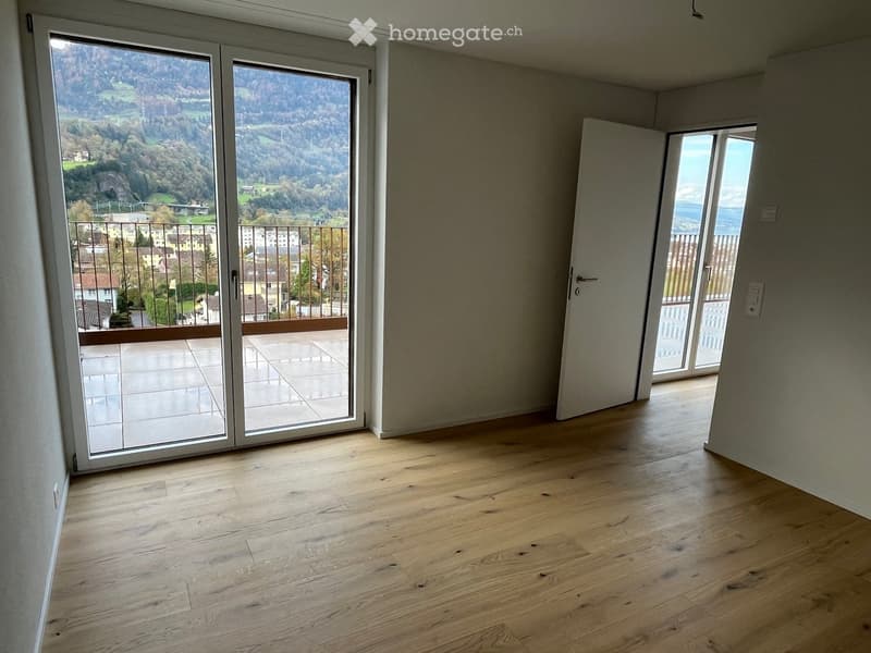 Empty room with wooden flooring, large sliding glass doors leading to a balcony with scenic mountain view.