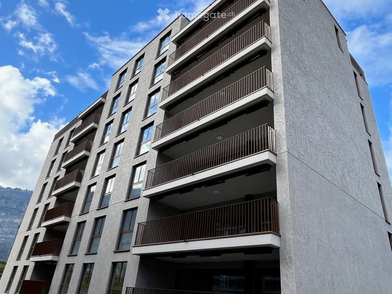 Modern multi-story apartment building with balconies and large windows, featuring a sleek concrete facade and contemporary design.