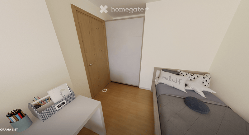 A small, modern bedroom with a single bed, a laptop on a small table, and a cup with pencils nearby. The room features light-colored walls and wooden flooring.