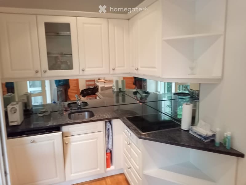 Modern kitchen with white cabinets, black countertops, stainless steel sink, and various appliances.