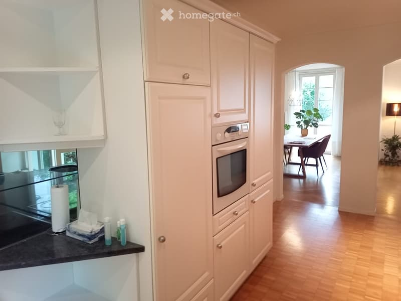 Modern kitchen with white cabinets, built-in oven, and a black countertop. The kitchen is connected to a dining area with a table and chairs.