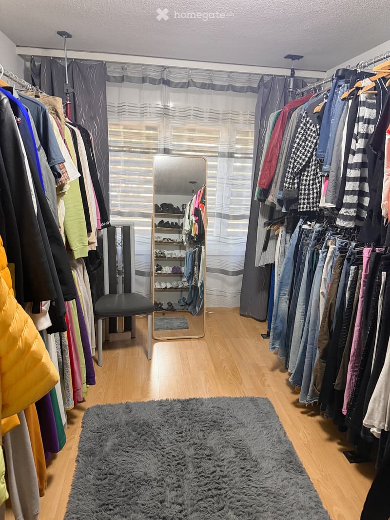 Well-organized walk-in closet with wooden flooring, multiple clothing racks, a large mirror, a small stool, and a fluffy rug.
