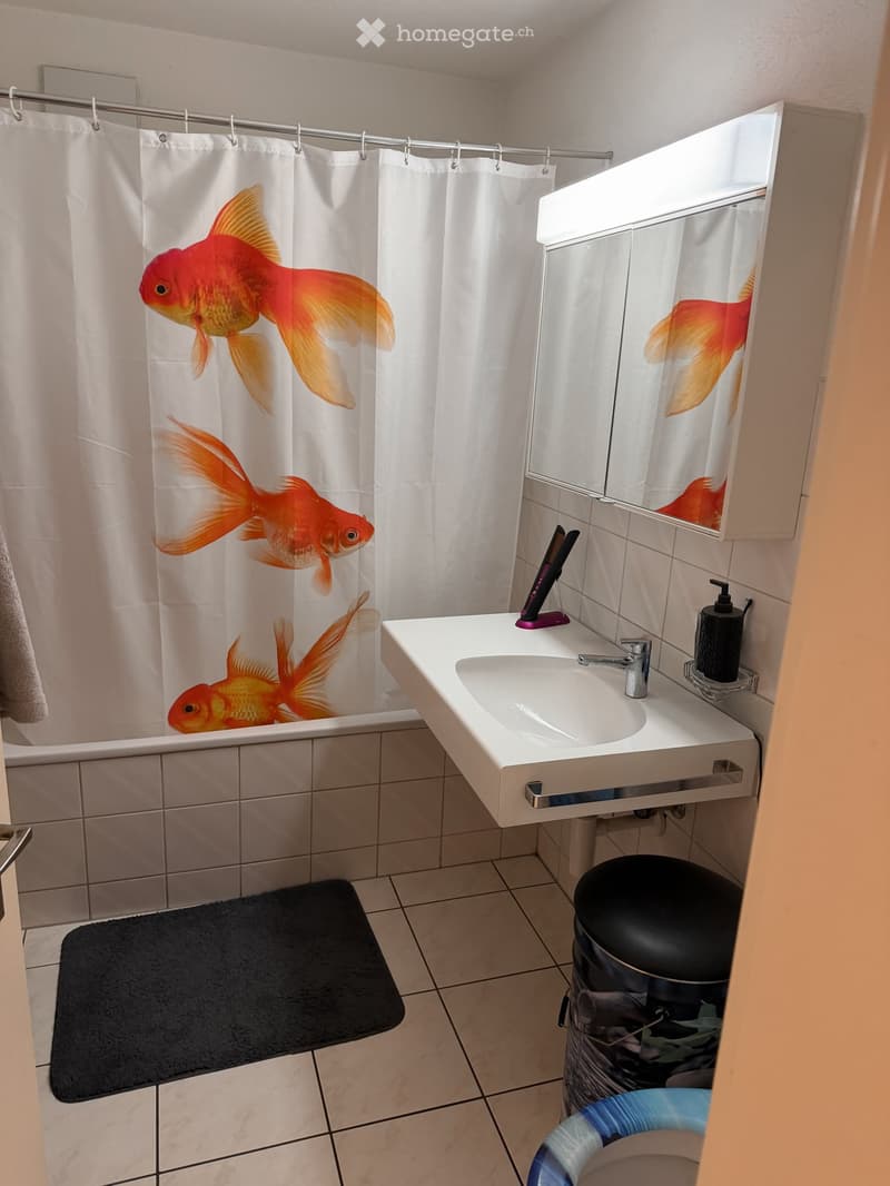 Bathroom with white tiles, a sink with a mirror cabinet, a shower curtain with goldfish design, and a black bathroom mat.