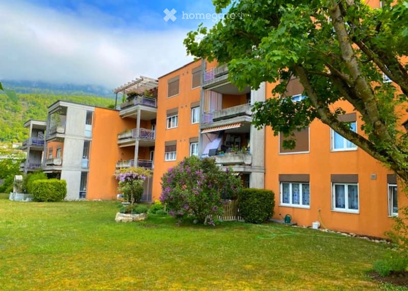 Multi-story apartment building with orange facade, balconies, and surrounding greenery.