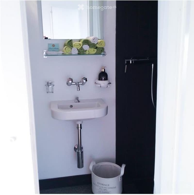 small bathroom with white sink, mirror, black shower curtain, soap dispenser, folded towels, trash bin