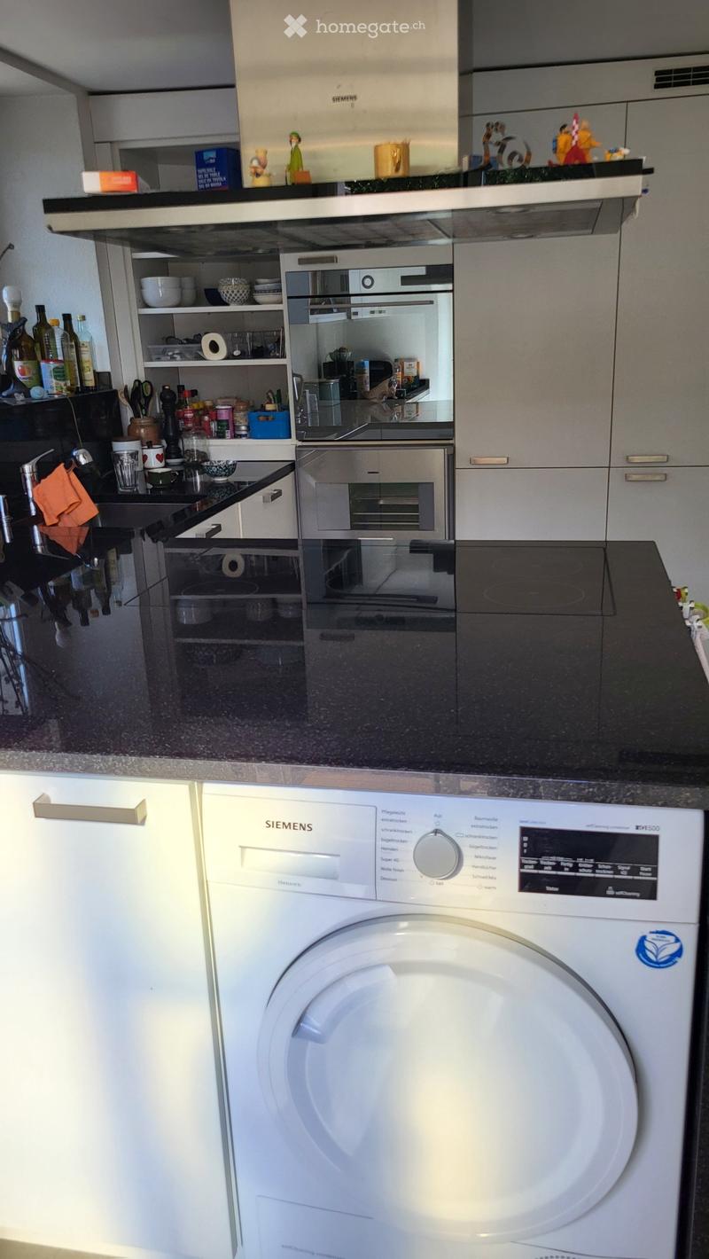Modern kitchen with stainless steel appliances, including an oven, dishwasher, and sink. Cabinets and shelves hold various kitchen items, including bowls, bottles, and a cup.