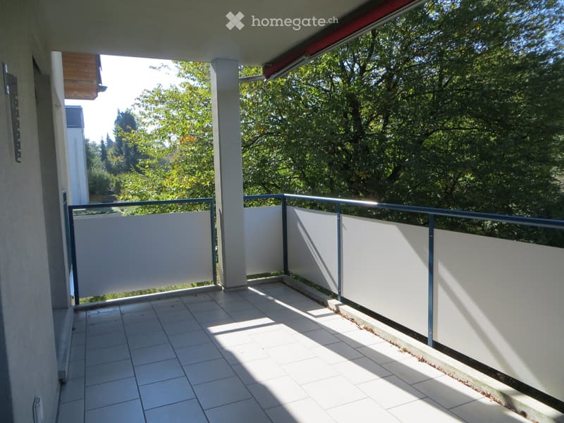 Balcony with tiled floor, white privacy screens, metal railing, and a view of green trees.