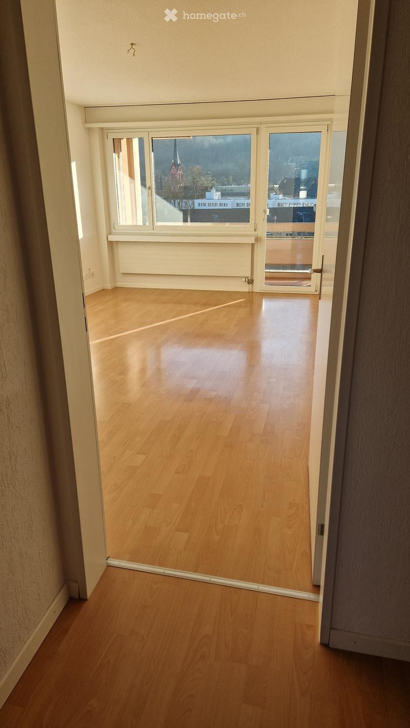 Empty room with wooden flooring, large windows, and a sliding glass door leading to a balcony.