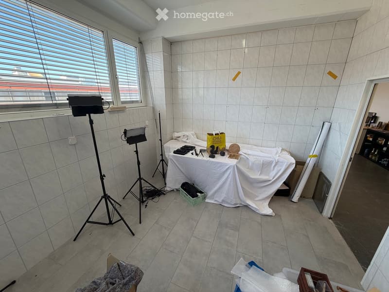 A room with tiled walls and floor, a table covered with a white cloth, a tripod with cameras, a shopping bag, and a stool.
